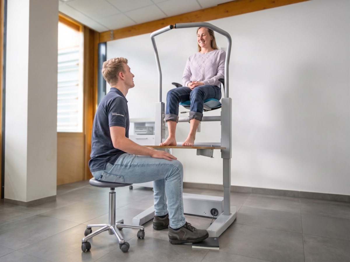The practitioner sits down on a stool with the legs tucked under the raised platform.